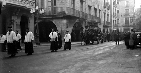 Seguici fúnebre d'un enterrament al seu pas per la plaça del Vi. Al centre, el carruatge fúnebre tirat per cavalls engalanats. 1920