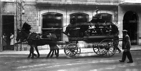 Carruatge fúnebre tirat per cavalls engalanats circulant per la plaça del Vi a l'altura de l'ajuntament de Girona. 1920