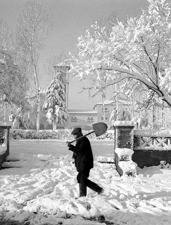 Després d'una nevada, un home camina amb una pala a la plaça de l'Assumpció al barri de Sant Narcís. Al fons, l'església. 13 de febrer de 1963