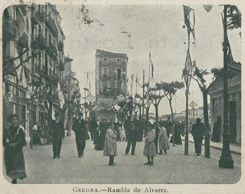 Vista de la part alta de la Rambla de la Llibertat, a l'altura de les casetes comercials Fèlix de Arzúa, engalanada durant una celebració. Al fons, els habitatges de la muralla del riu posteriorment enderrocats. 1901-1904