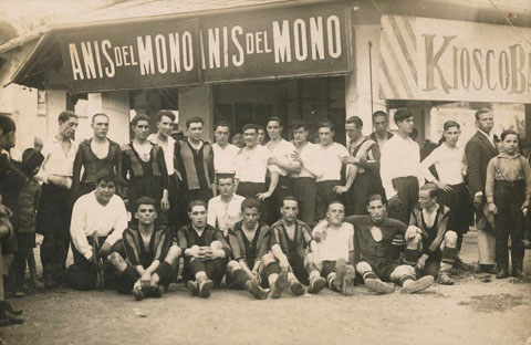 El quiosc d'en Montaña al camp de futbol de Vista Alegre de Girona. Al davant, dos equips de futbol. S'identifica a dalt: Sumsi I, Colls, Marquès, Pere Vila, Bosch, Gibert, Gadea, Salvi, Fàbrega, Teixidor, Casas, Ismael, Alvalat, Gauchia, Fernàndez, Rabas, Juanito i Montaña. A baix: Amadeu Oliva, Sumsi II, Quintana, Balançà, Pagès, Dalmau, Puig i Norat. 1921-1930
