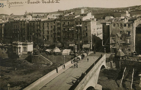 Vista des d'un punt elevat del pont de Pedra. A l'esquerra s'hi observa el quiosc de revistes, i a tocar el Dispensari Municipal, el quiosc de l'urinari. A la dreta, el quiosc de begudes. 1918-1924