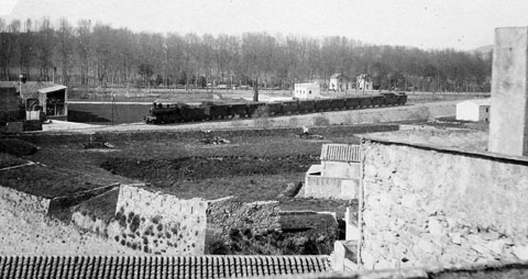 Vista de la Devesa des del baluard de la Santa Creu. En primer terme, les restes del baluard. En segon terme, un tren circulant pel terraplè del tren a l'altura del carrer Bonastruc. 1903