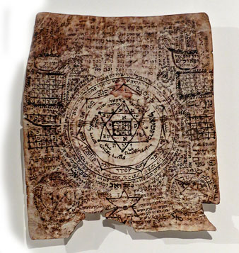 Amulet hebreu. Tinta negra sobre pergamí. Segle XVIII, Europa de l'Est. A les comunitats jueves medievals era molt comú l'ús d'amulets que tenien la funció de protegir tant la mare que paria com la criatura que naixia. En aquest s'hi veuen combinacions de lletres de l'alefat que configuren noms divins i d'àngels protectors i s'hi llegeix l'expressió 'ha-eix xaca ha-eix' (el foc s'enfonsa en el foc), un conjur de protecció en el moment del part