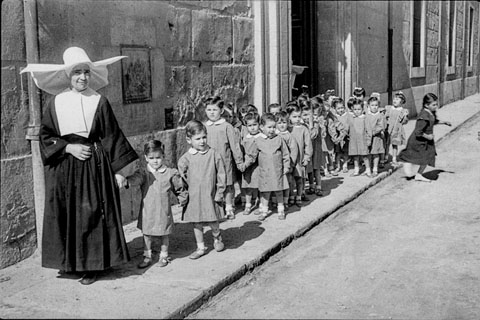 Una monja amb un grup de mainada a l'exterior de l'Hospici. 1950