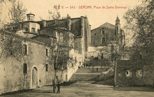 Vista parcial de la plaça de Sant Domènec amb l'edifici de les Àligues en primer terme a l'esquerra. Al fons, el convent de Sant Domènec utilitzat com a caserna militar. 1900