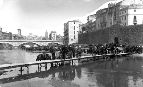 El mercat del bestiar a l'Areny, davant el tram de muralla del Pes de la Palla. Al centre, la palanca d'en Vila, que salvava el riu Onyar i comunicava el portal de l'Àngel, a la dreta, amb l'altre banda del riu. 1880-1890