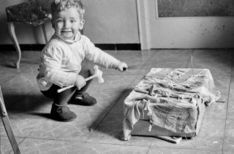 Jordi Prat a l'interior de l'habitatge familiar del carrer Ciutadans de Girona amb un martell de joguina i una caixa tapada amb un drap, fent cagant el Tió durant les festes de Nadal. 1967