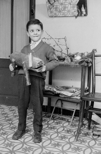 Retrat d'un nen en un interior amb un Tió de Nadal a les mans. 1960