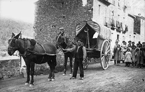 Retrat d'un home amb una tartana en un carrer. Al fons, un grup de nens. 1910