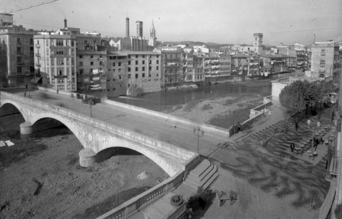 Vista enlairada del Pont de Pedra. Entre la xemeneia de la Gròber i el campanar neogòtic de Santa Susanna, s'observa la Torre de les Aigües