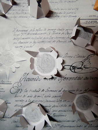 Al centre: document gironí del segle XIX amb el segell que l'autentifica embolcallat de paper retallat i plegat (rèplica). A l'entorn, treballs de Pericot que hi són inspirats